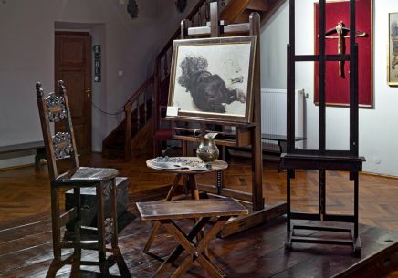 Pracownia domowa Jana Matejki. Na niskim drewnianym podeście stoją meble, przy których pracował artysta. To drewniane krzesło lombardzkie z roślinnymi ornamentami, stolik z paletą i dzbankiem oraz dwie sztalugi. Na jednej z nich jest rozmazany obraz.